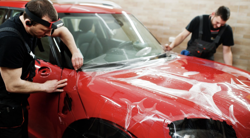 兩位技師在室內工作室為紅色轎車引擎蓋黏貼透明保護膜,確保膜料平整服貼