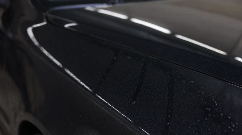 黑色汽車漆面近距離特寫，呈現水滴在塗層上形成的撥水效果與細緻的漆面紋理